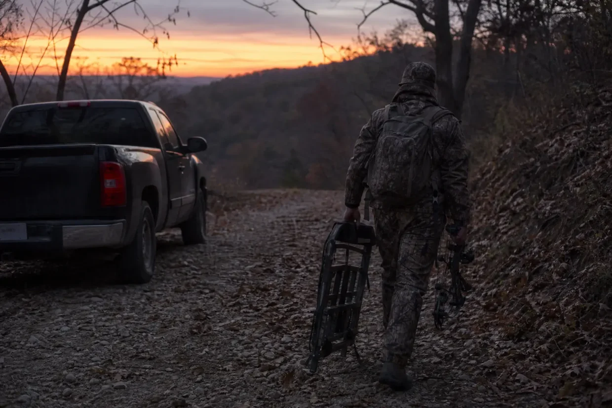 Camouflaged person in helmet pushes a bicycle along a rocky road beside a parked pickup at sunset