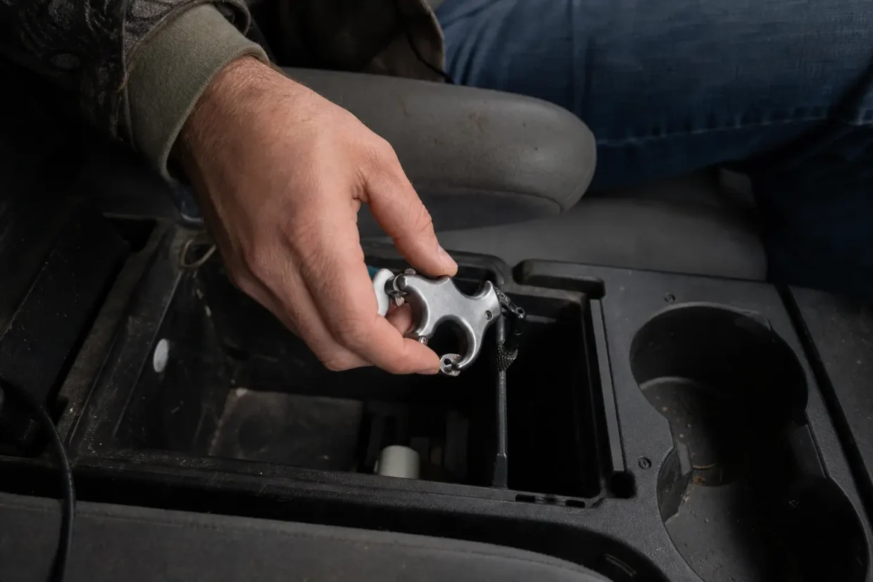 Hand reaching into an open vehicle compartment holding a small metallic revolver-like handgun