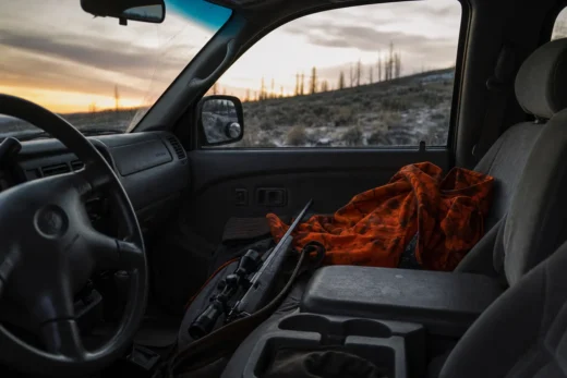 Interior view of a car with an orange blanket on the passenger seat and a rifle resting near the center console