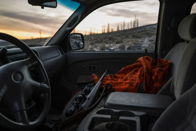 Interior view of a car with an orange blanket on the passenger seat and a rifle resting near the center console