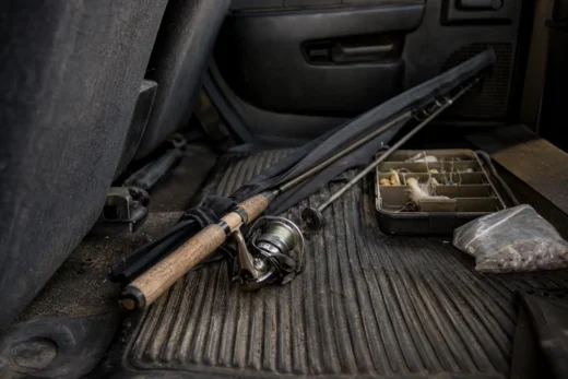 Fishing rod handle, black strap, spinning reel, tackle box with compartments, and a plastic bag on a truck bed